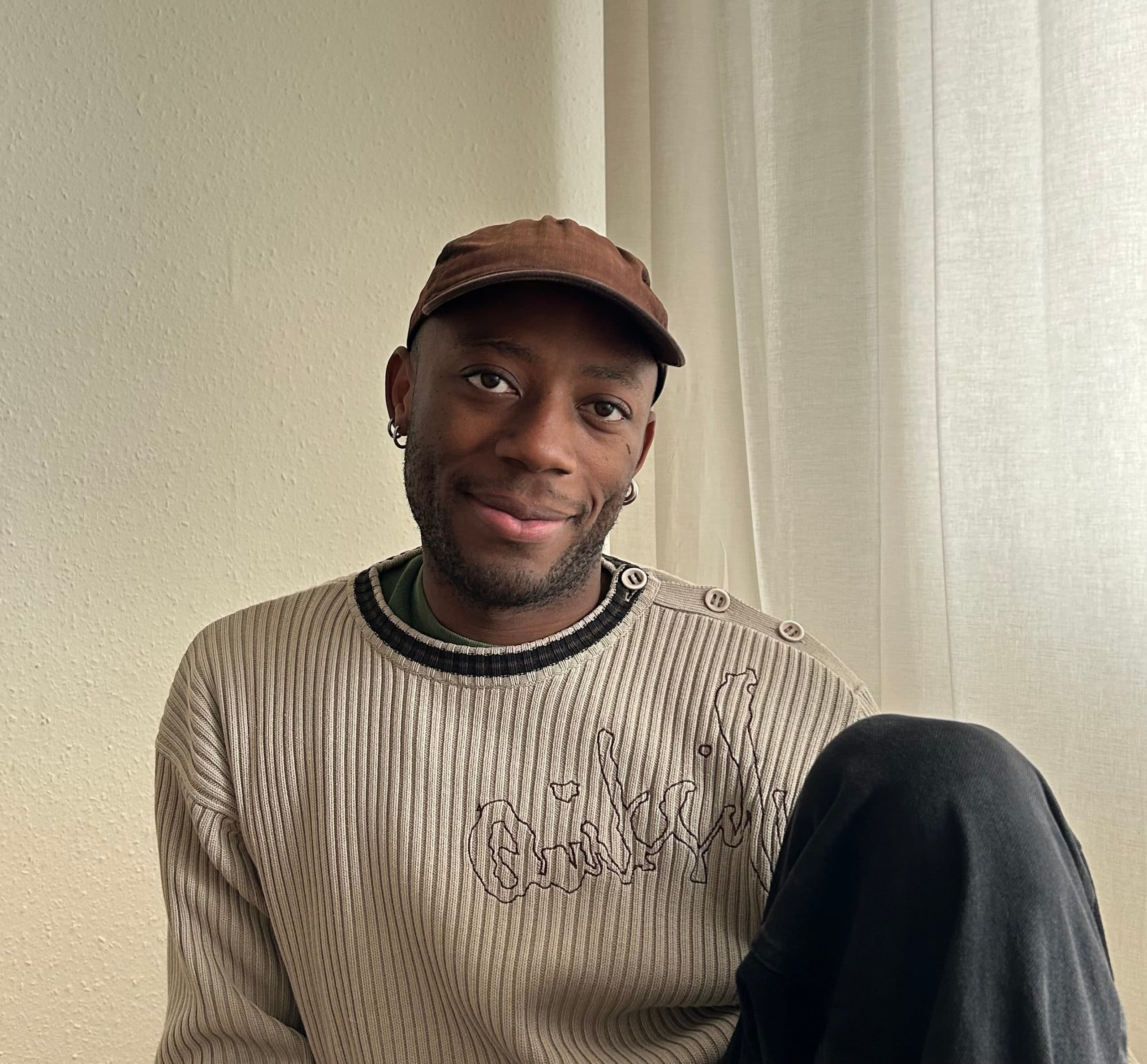 Portrait d'une personne assise portant une casquette et souriant légèrement.