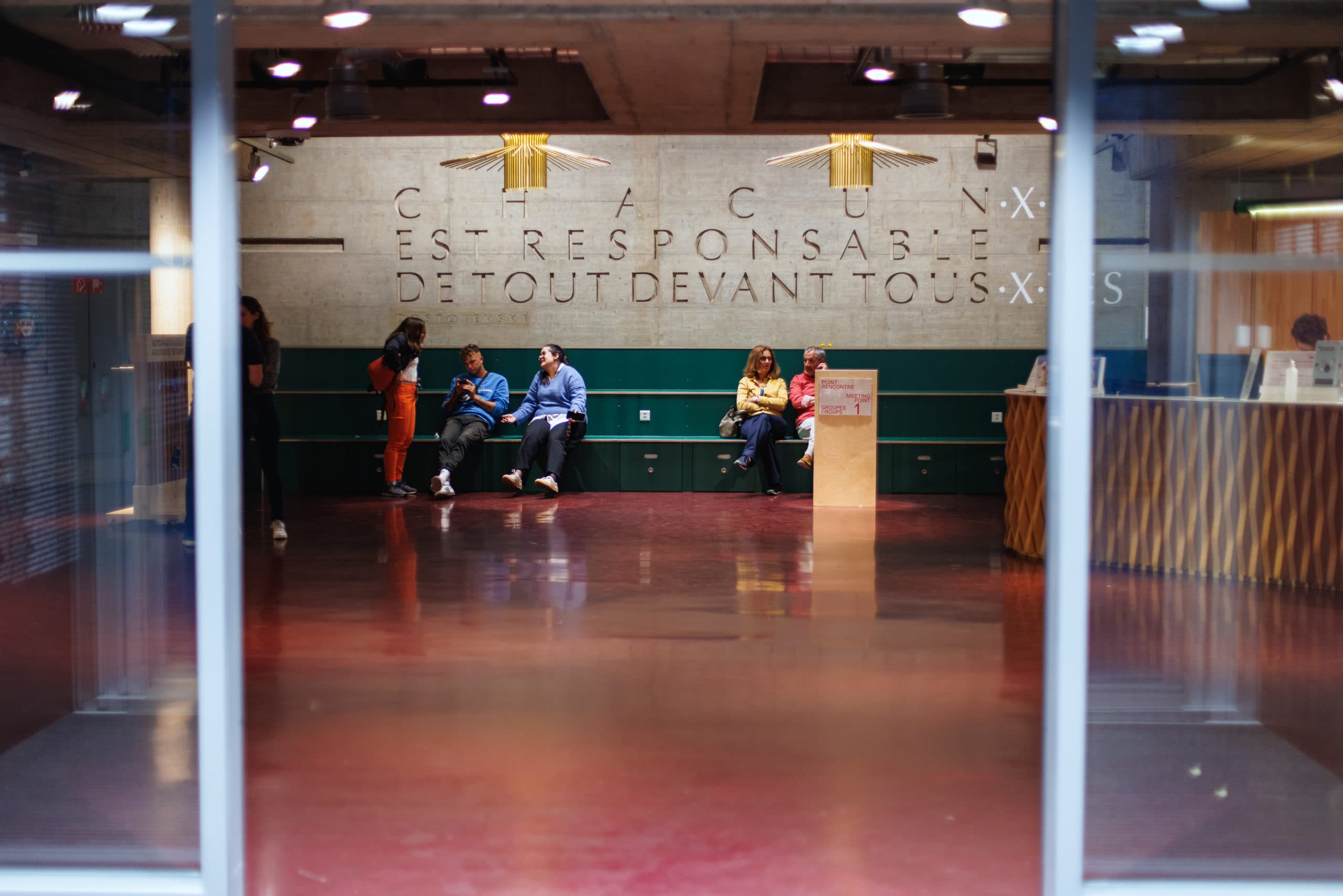 Espace d’accueil intérieur avec un comptoir et plusieurs personnes debout ou en train de circuler dans un hall moderne.