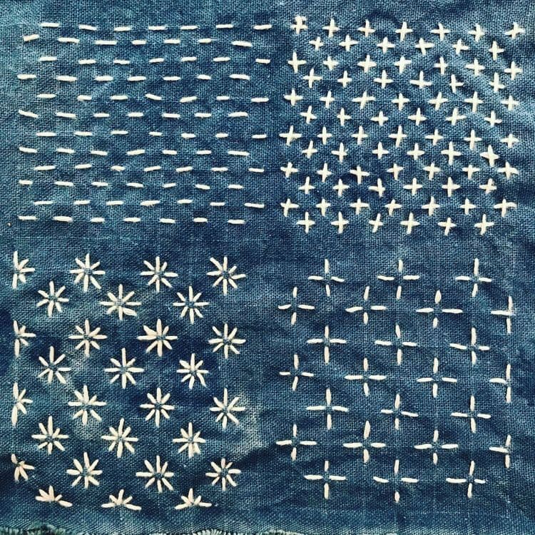 Points de broderies sashiko en forme de croix, d'étoiles ou de traits sur faits avec un fil blanc sur un tissus bleu indigo.