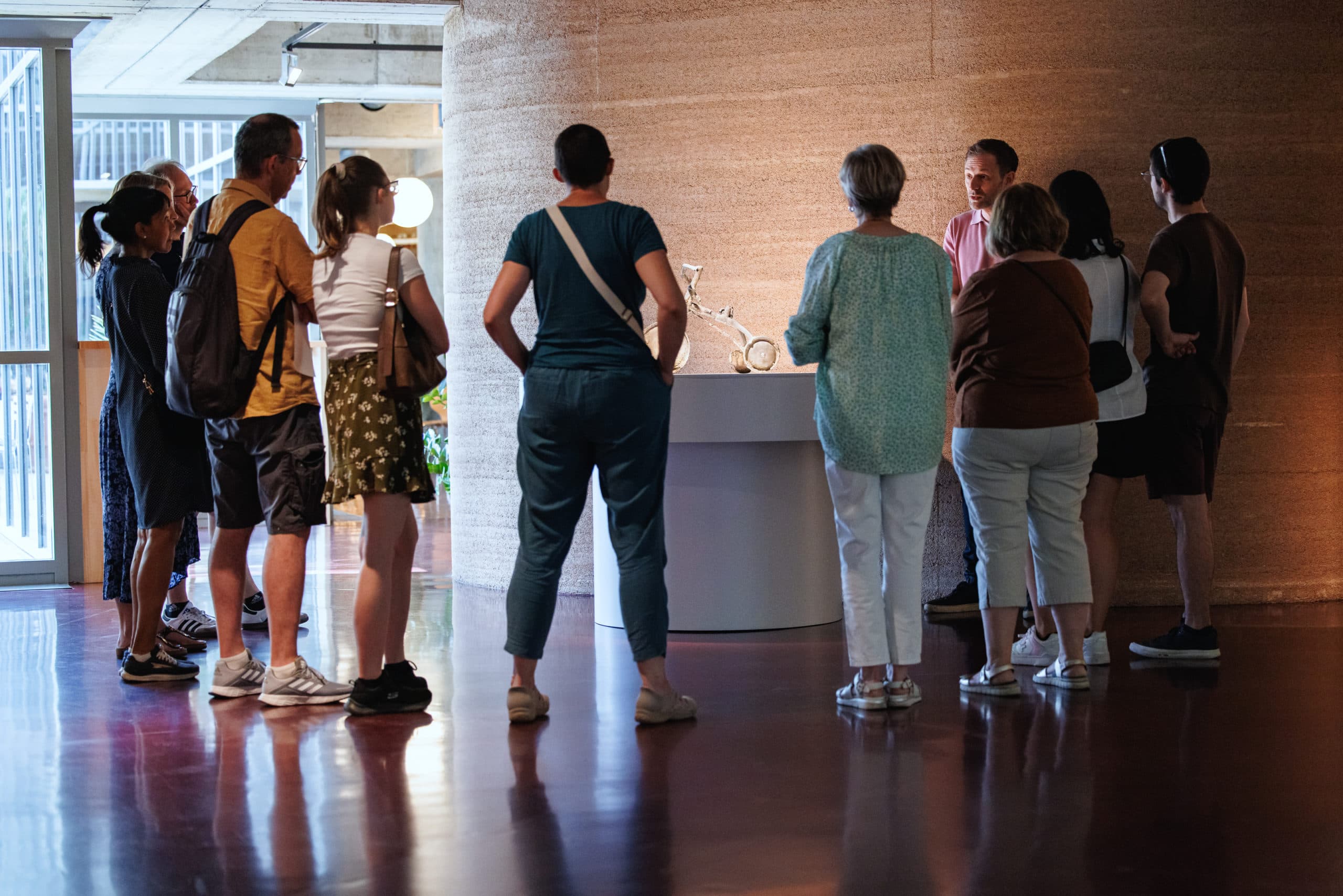 Un groupe d’une dizaine de personnes se tient debout dans une salle d’exposition, rassemblé autour d’une œuvre éclairée et écoutant une présentation